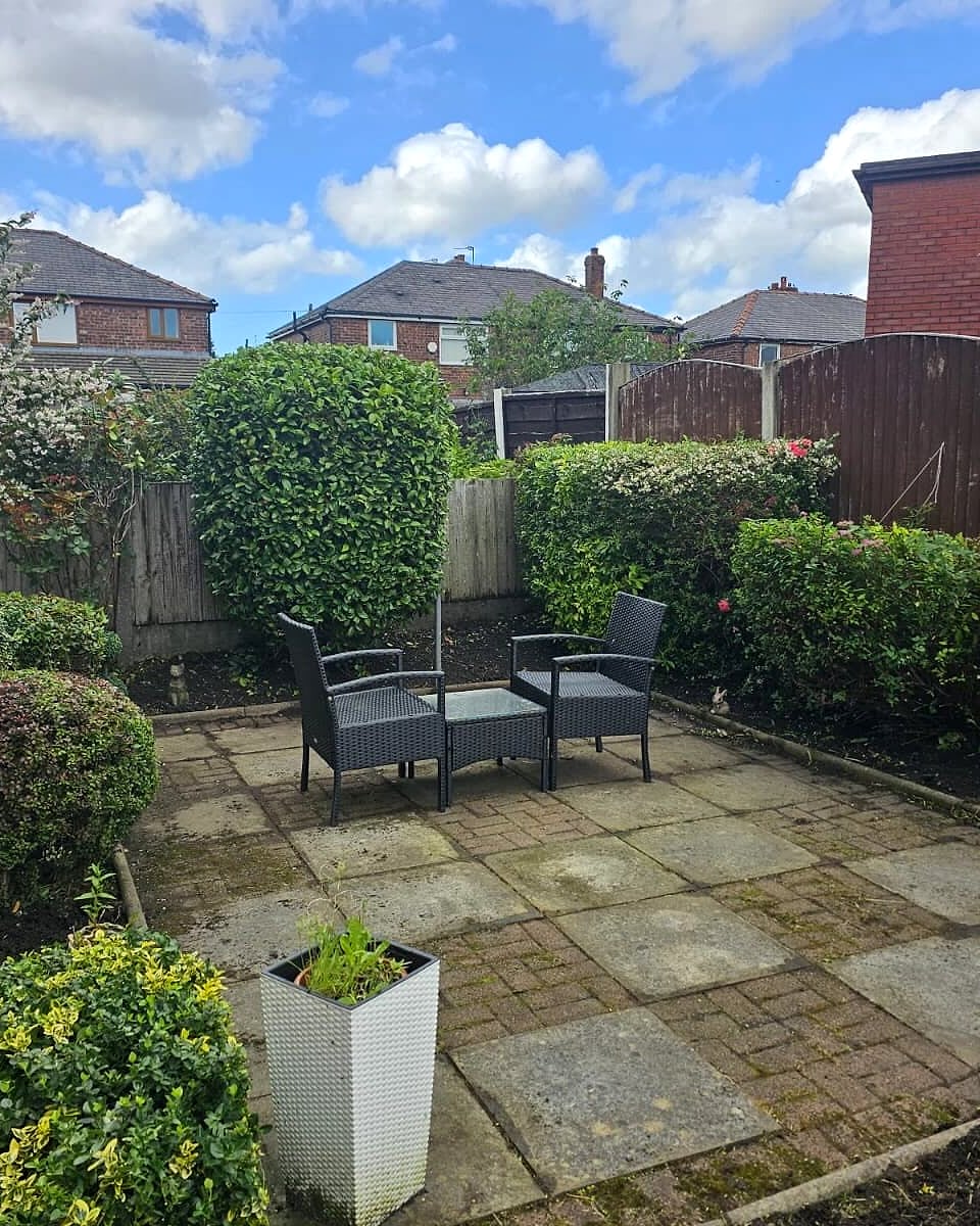 The same back garden after: clear patio with seating and neatly shaped shrubs